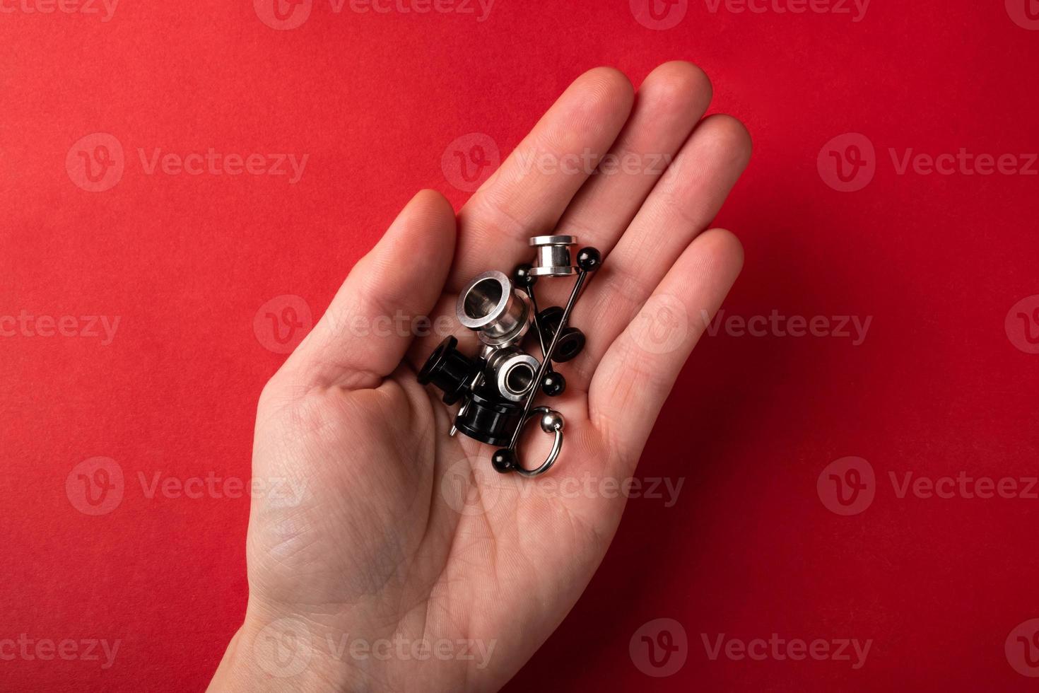 Piercing and jewelry for the ears in the palm of the hand on a red background photo