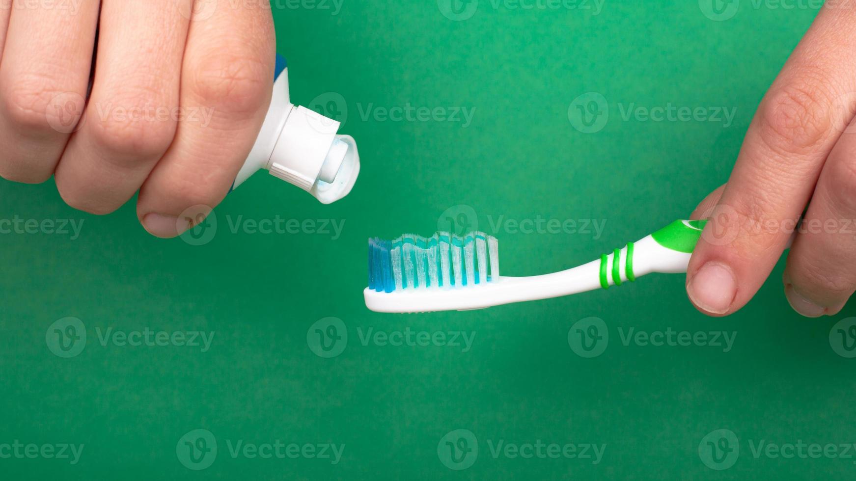 Hand squeezes toothpaste onto a toothbrush on a green background close-up photo