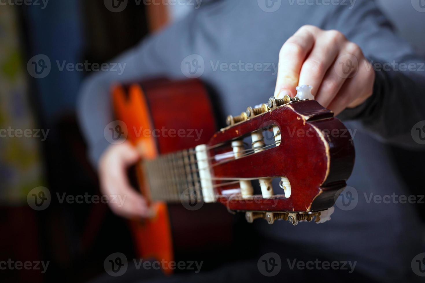 The musician tunes an acoustic six-string guitar photo