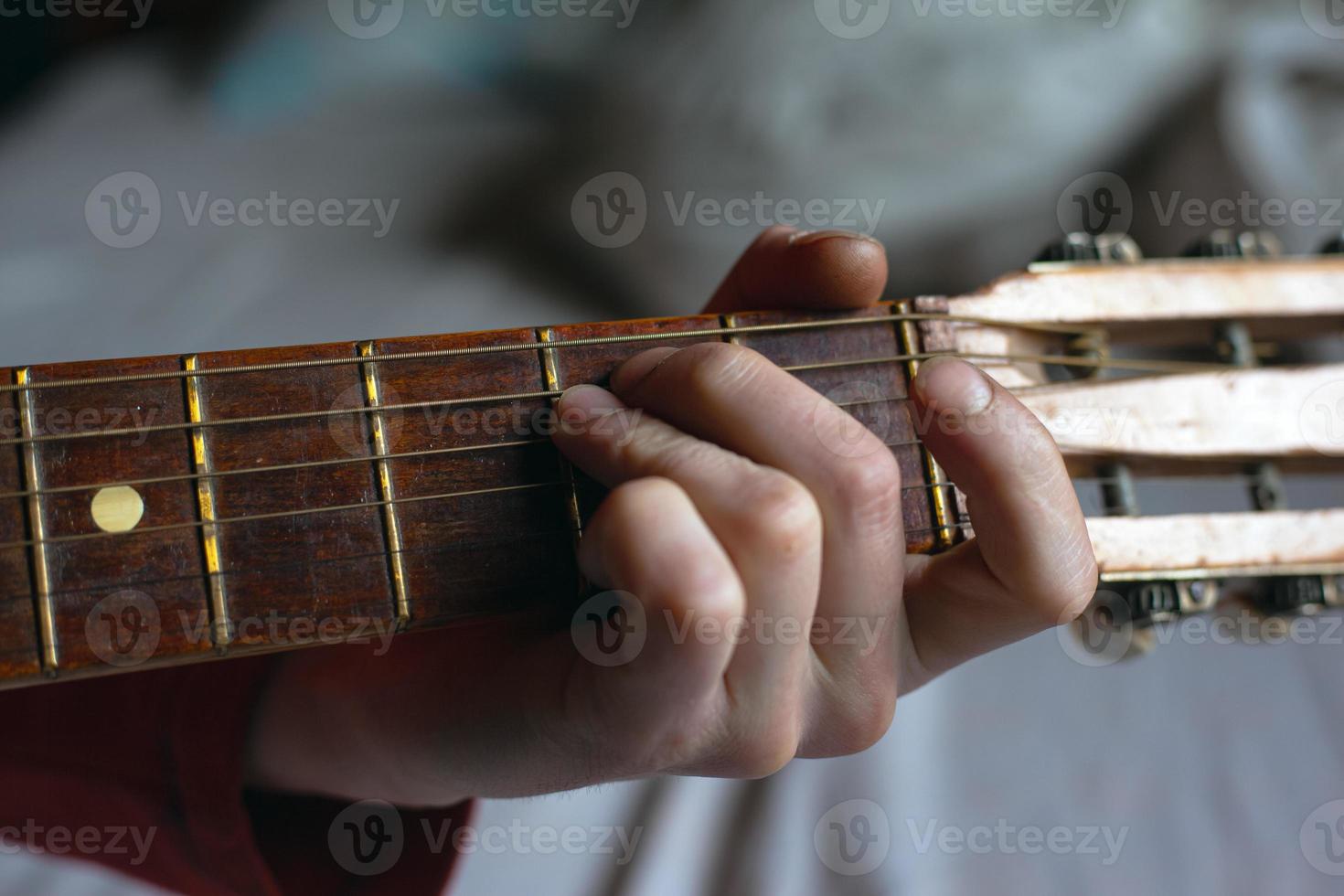 Guy plays a melody on an acoustic guitar while holding his hand on the fretboard photo