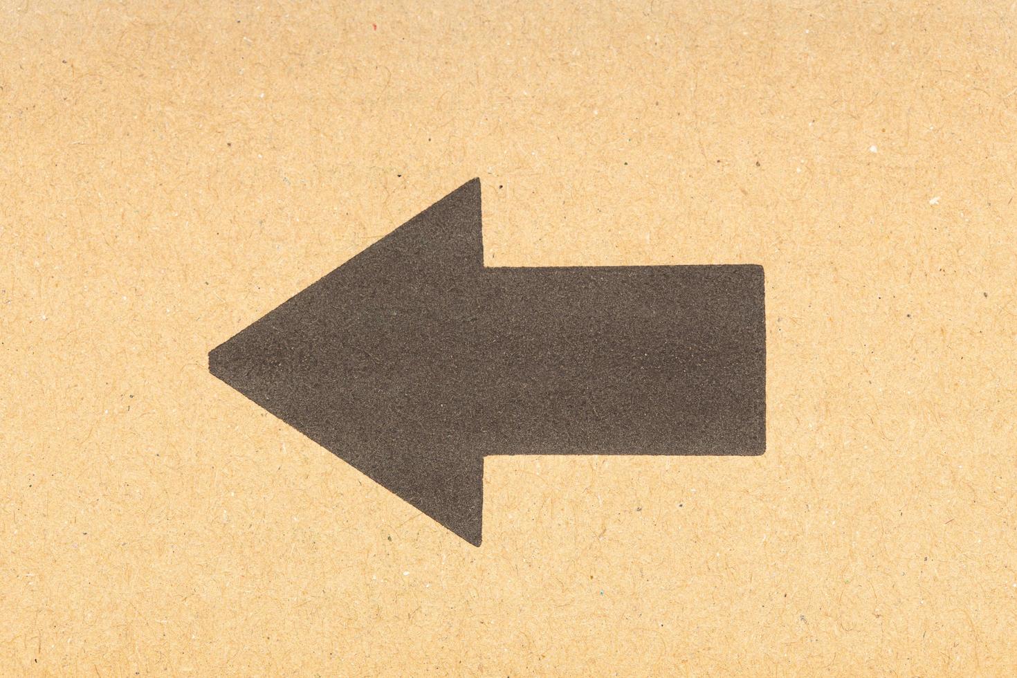 Black arrow pointing left on brown cardboard background photo