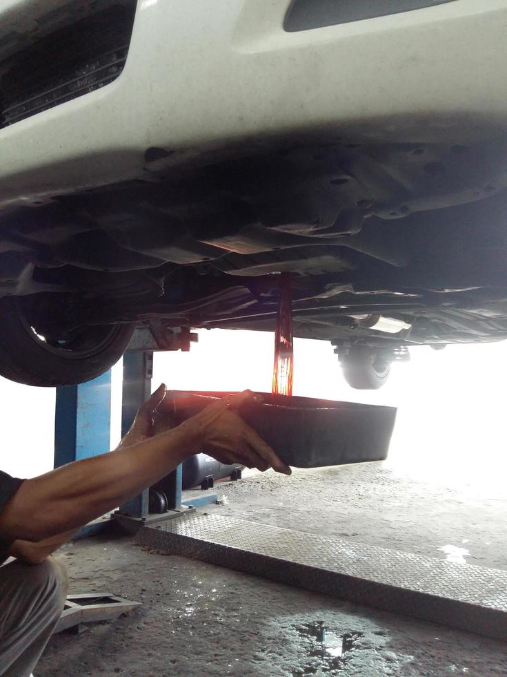 Mechanic draining engine oil from a car photo