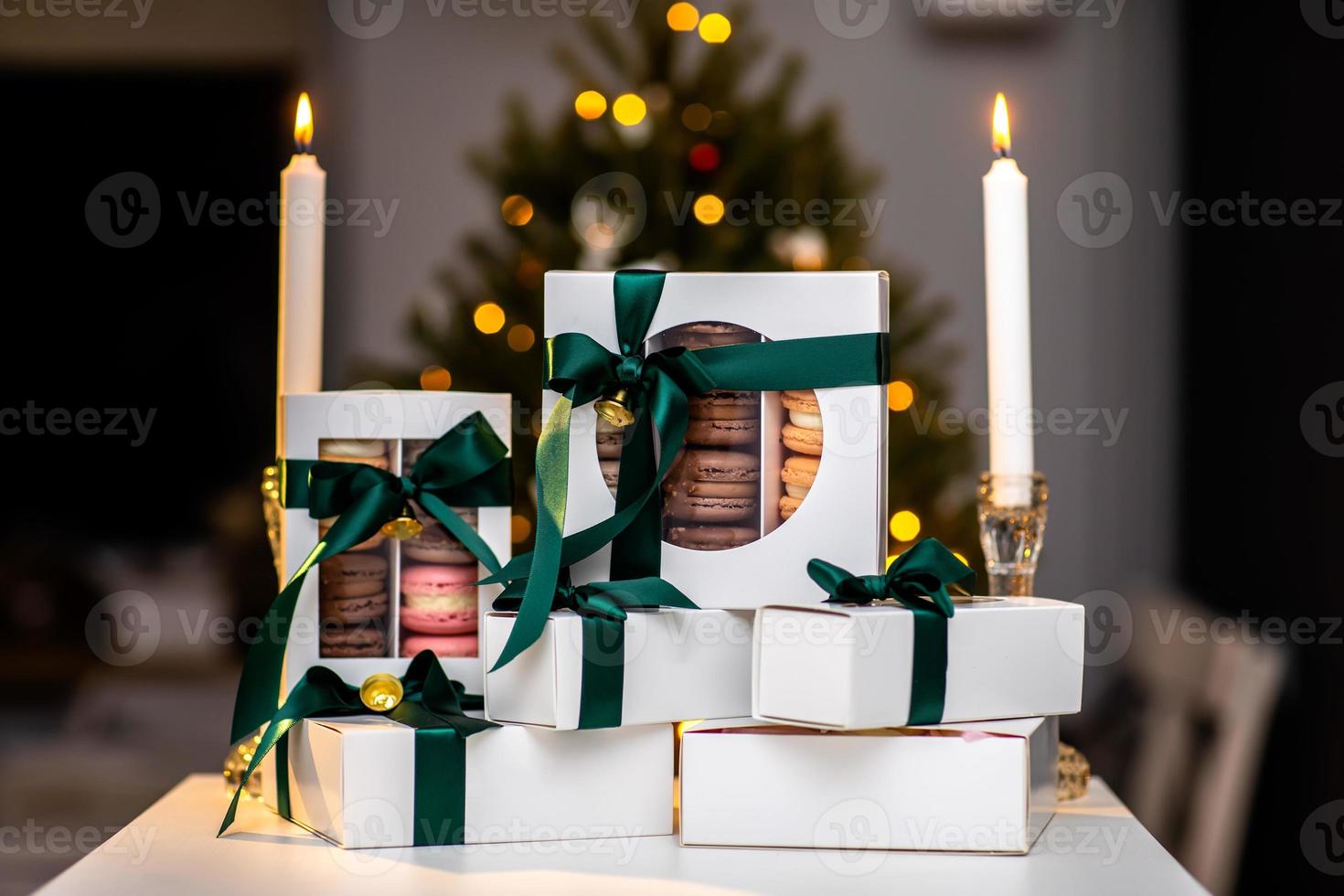 macarrones franceses en cajas blancas con cinta verde. árbol de Navidad con bokeh y velas en el fondo. cocina francesa europea moderna. tema de navidad, tarjeta de feliz navidad. humor de año nuevo. foto