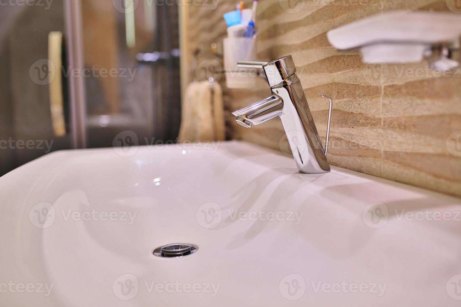 Mezclador de grifo de lujo en un lavabo blanco en un hermoso baño interior gris. Vista de cerca del bonito grifo de metal en el baño moderno foto