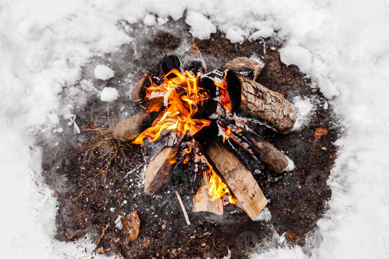 Campfire burns in the snow in the woods. Campfire burning in cold winter. Snow, forest and fire. Winter. Tourism. Flames on snow. Winter background. Nature. photo