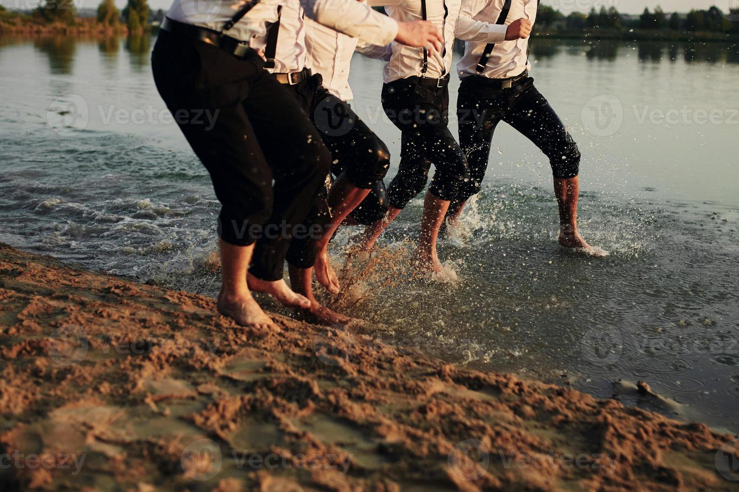 pies de hombres en el agua. hombres disfrazados corren sobre el agua. se están divirtiendo, jugando y salpicando agua a su alrededor. verano. Grupo de pies de hombres jóvenes felices salpicar agua en el mar y rociar en la playa foto