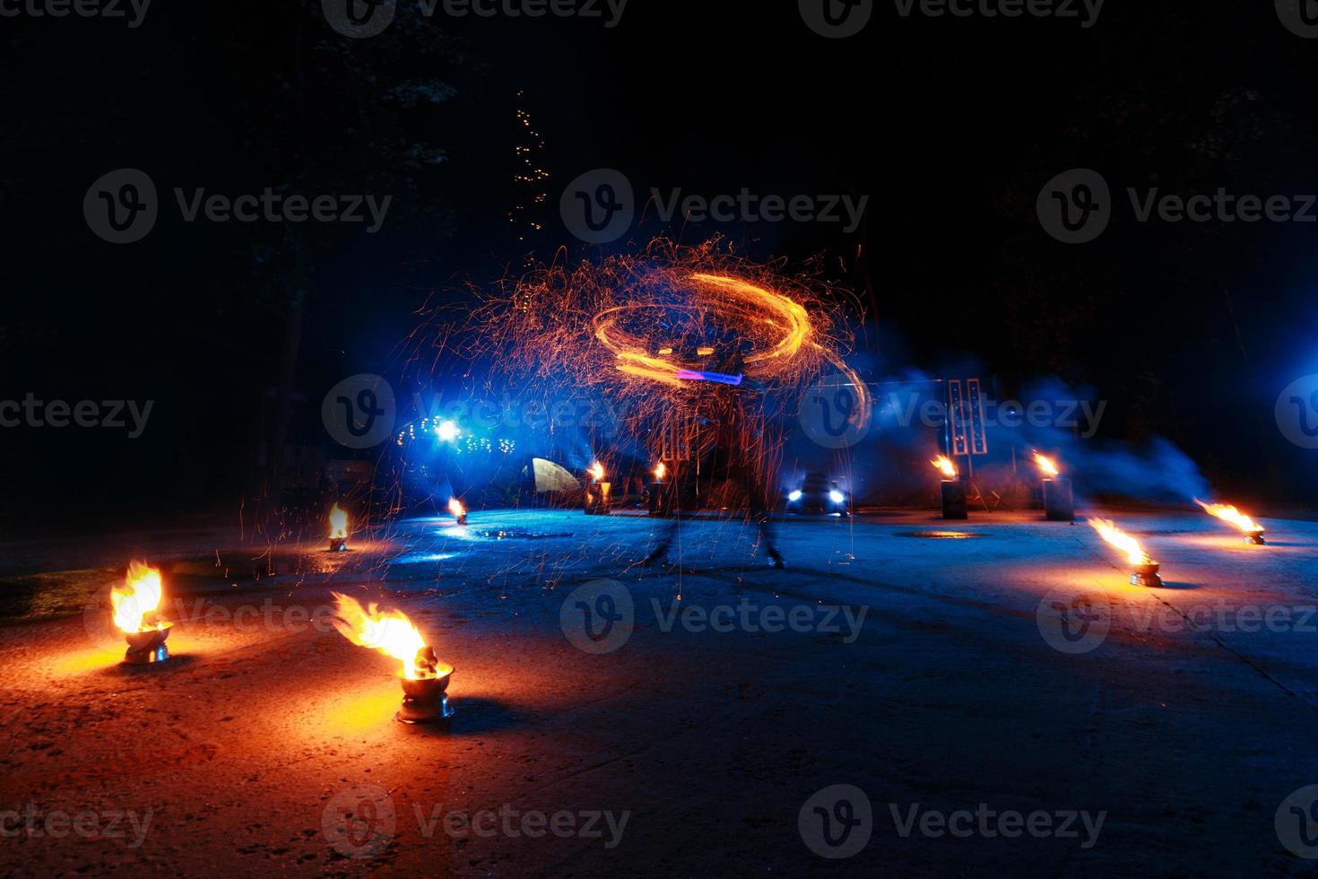 espectáculo de fuego, baile con llamas, maestro masculino haciendo malabares con fuegos artificiales, actuación al aire libre, dibuja una figura ardiente en la oscuridad, chispas brillantes en la noche. un hombre en un traje llevó a bailar con fuego foto