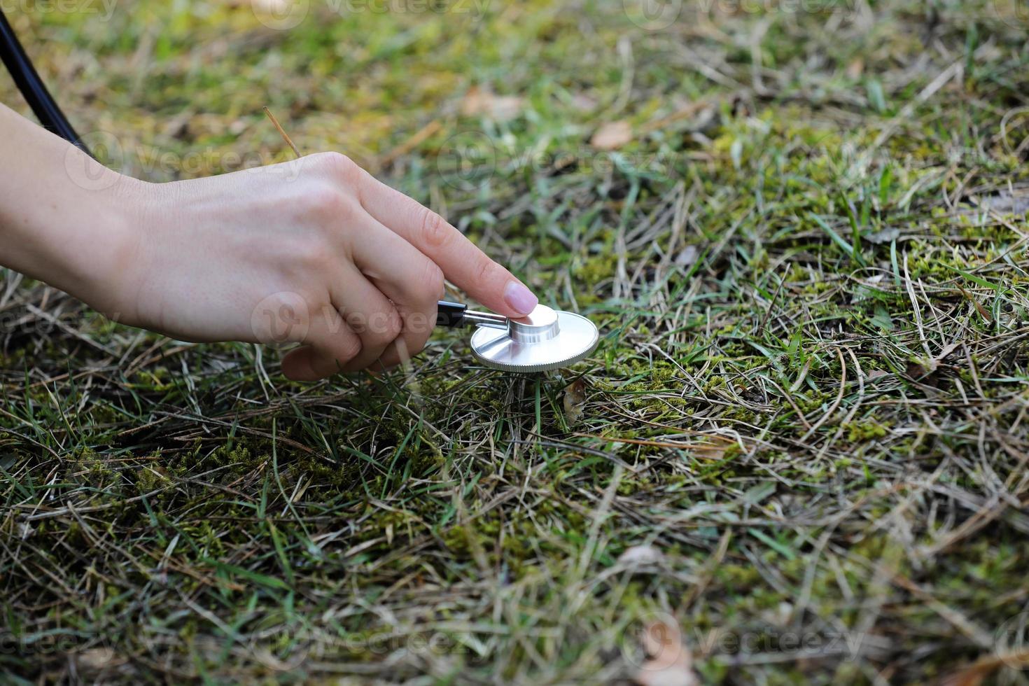 mano de una mujer está escuchando el suelo con un estetoscopio en el parque. concepto de amor al medio ambiente. enfoque selectivo. Copie el espacio. foto