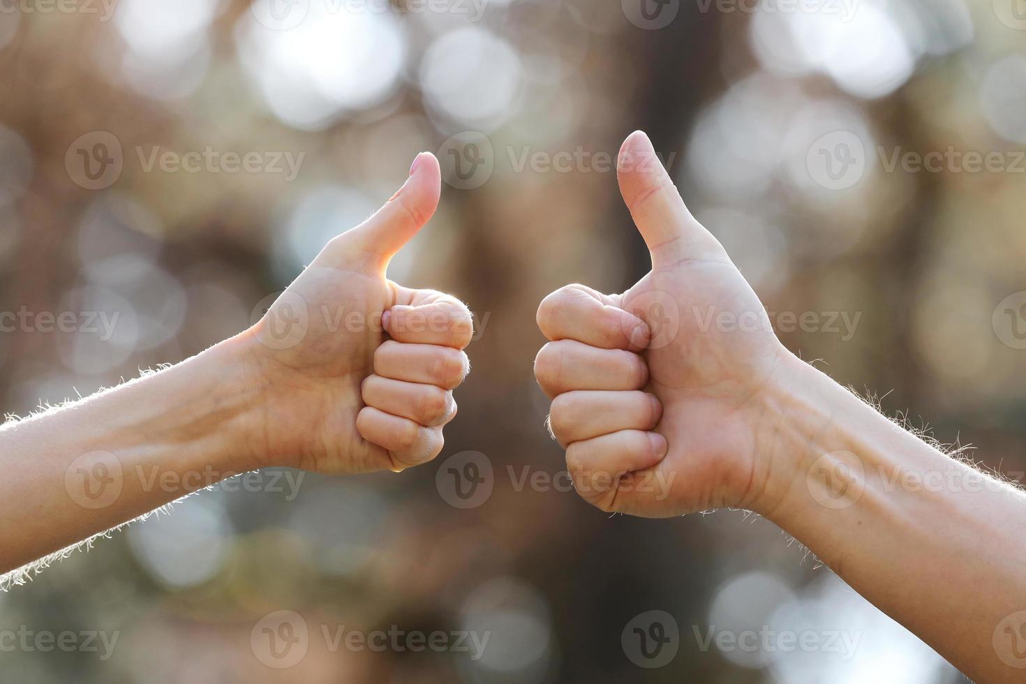 Male and female hands showing thumbs up outdoors. photo