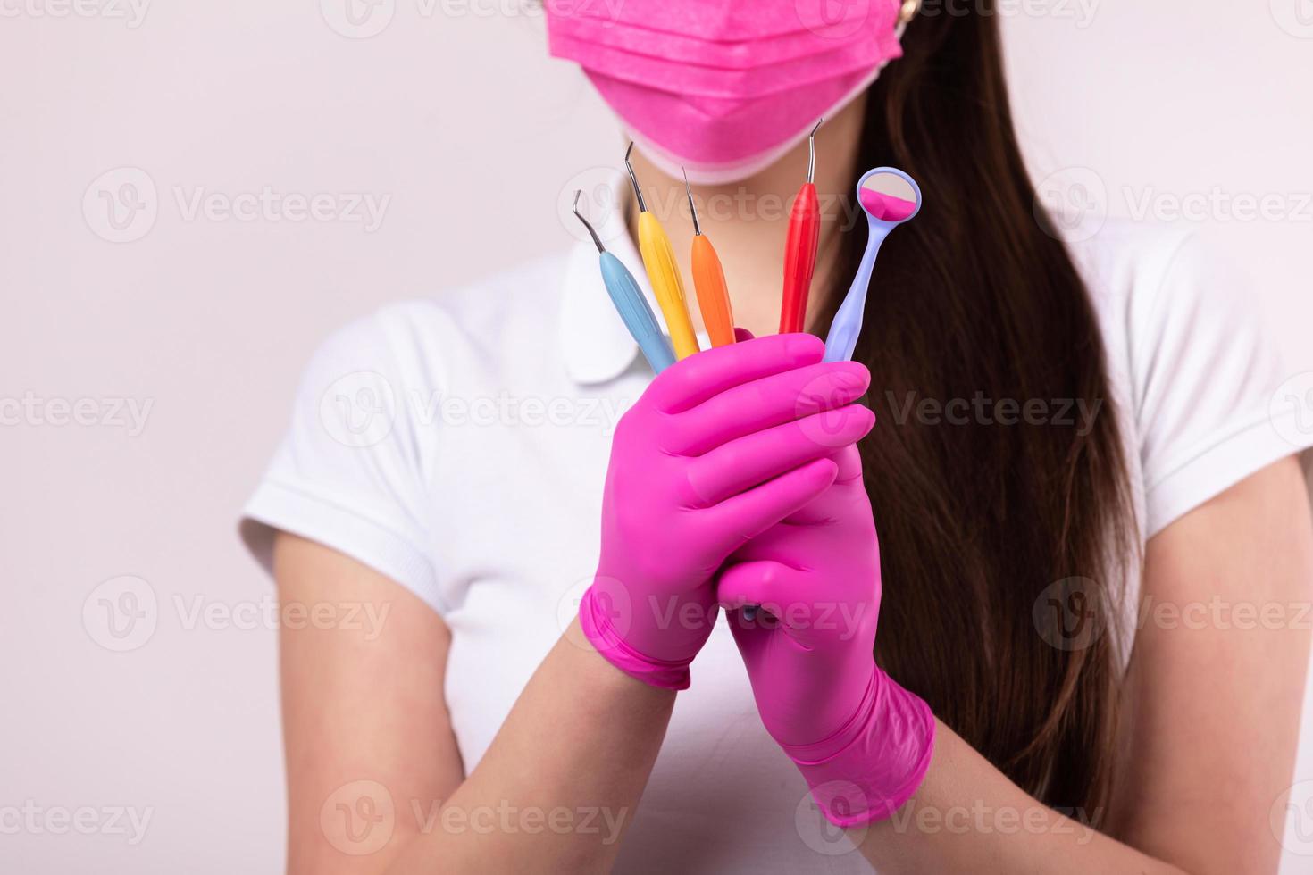 concepto de personas, medicina, odontología y salud - mujer dentista en mascarilla rosa y guantes médicos con herramientas de colores sobre fondo blanco. dentista para niños foto