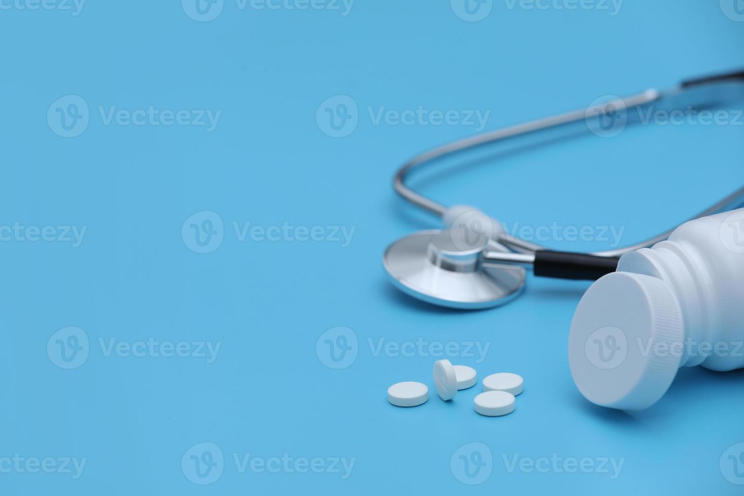 Pills spilling out of pill bottle syringe thermometer and stethoscope on blue background. Selective focus. Ideal for medical and healthcare concept photo