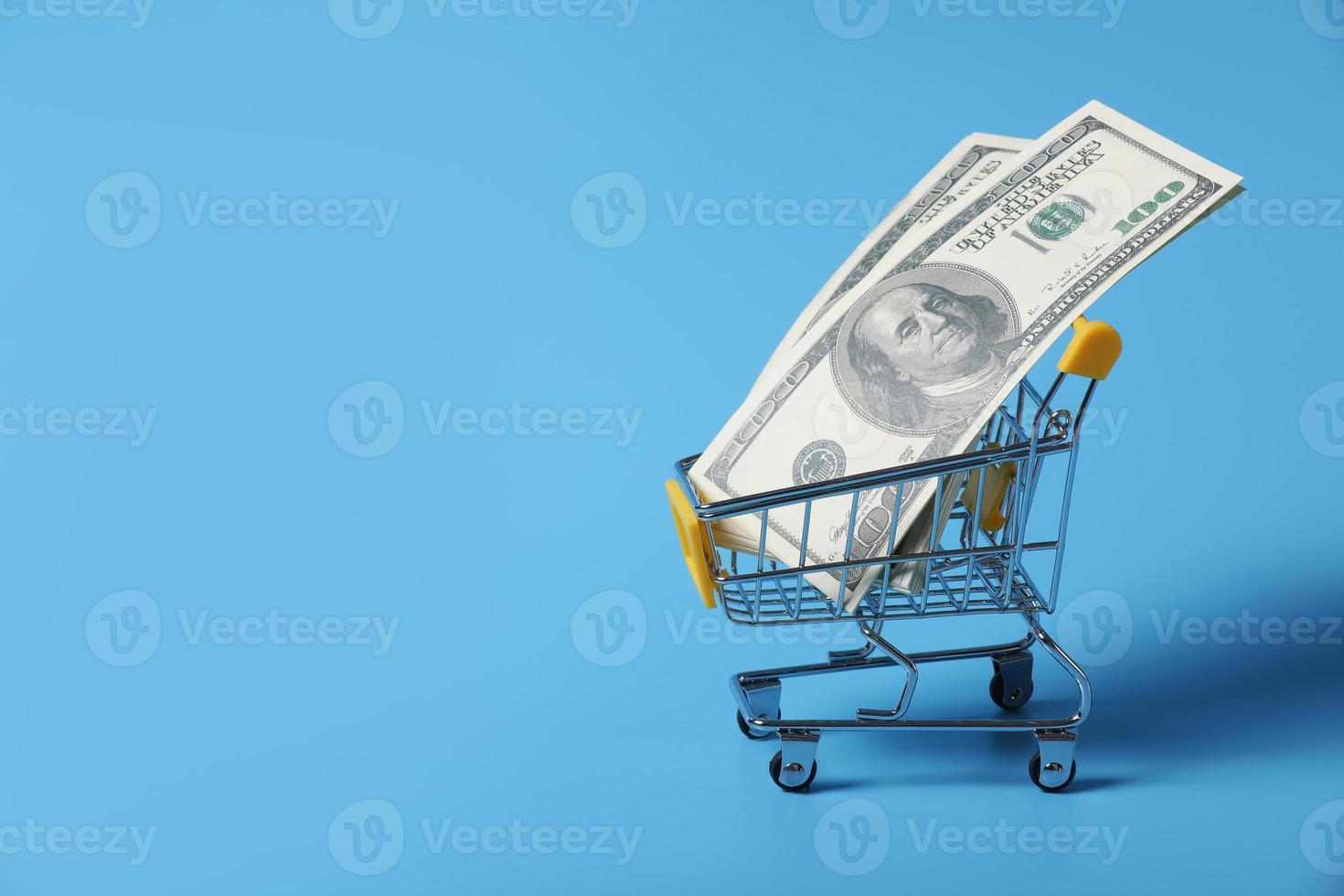 Dollar bills in shopping cart on shopping isolated on a blue background. close-up of shopping trolley. Medicine concept with copy space photo