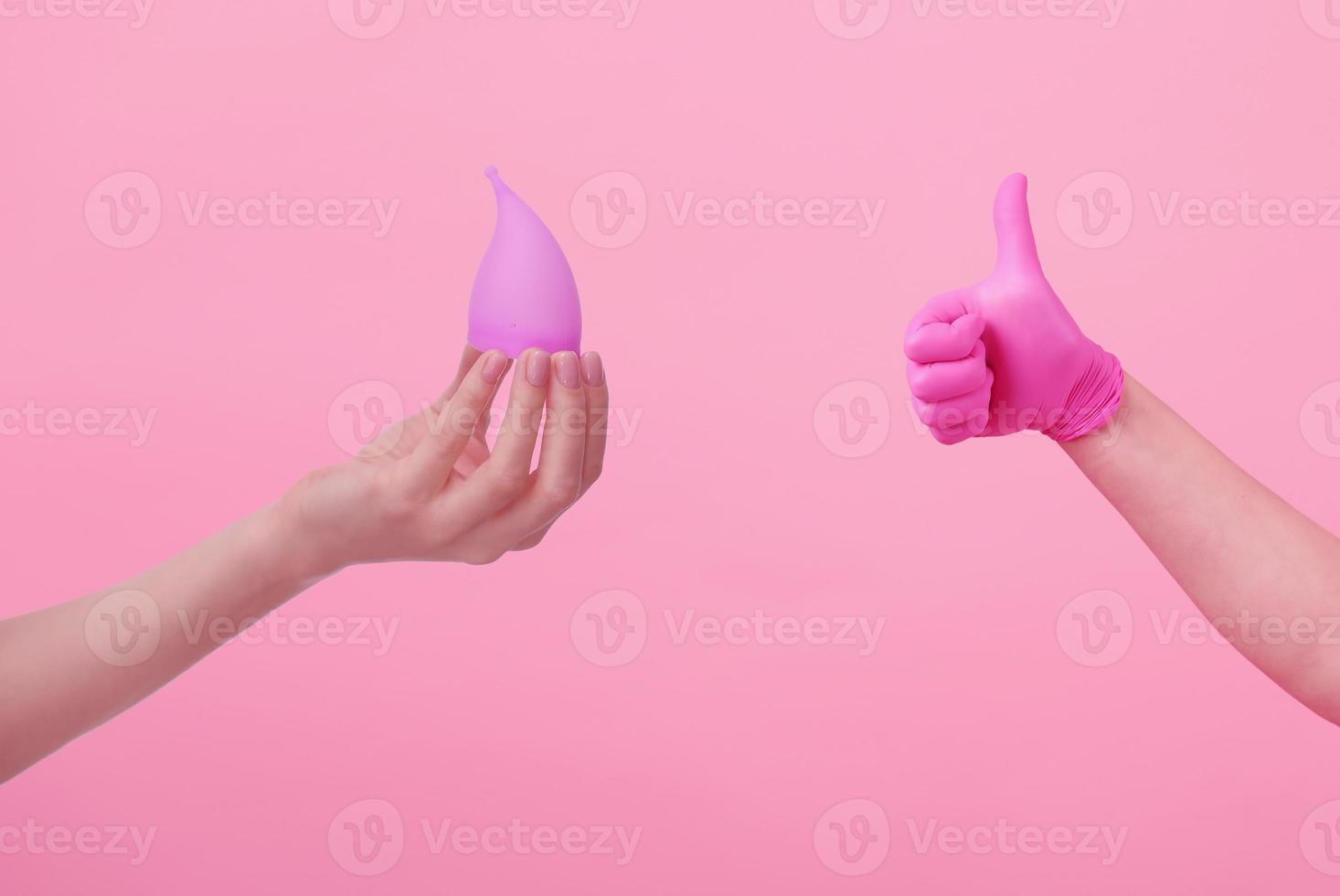 Hands of a young woman in pink latex gloves and hand with a menstrual cup on pink background. Women's health. Preservation of ecology. Waste-free use. Women's hygiene products. photo