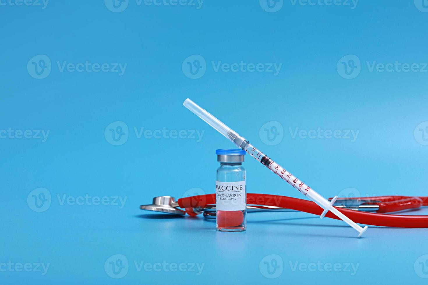 Medicine bottle with coronavirus vaccine covid-19. Medical glass vial, stethoscope and syringe for vaccination. Liquid vaccine in laboratory, hospital, or pharmacy concept isolated on blue background. photo