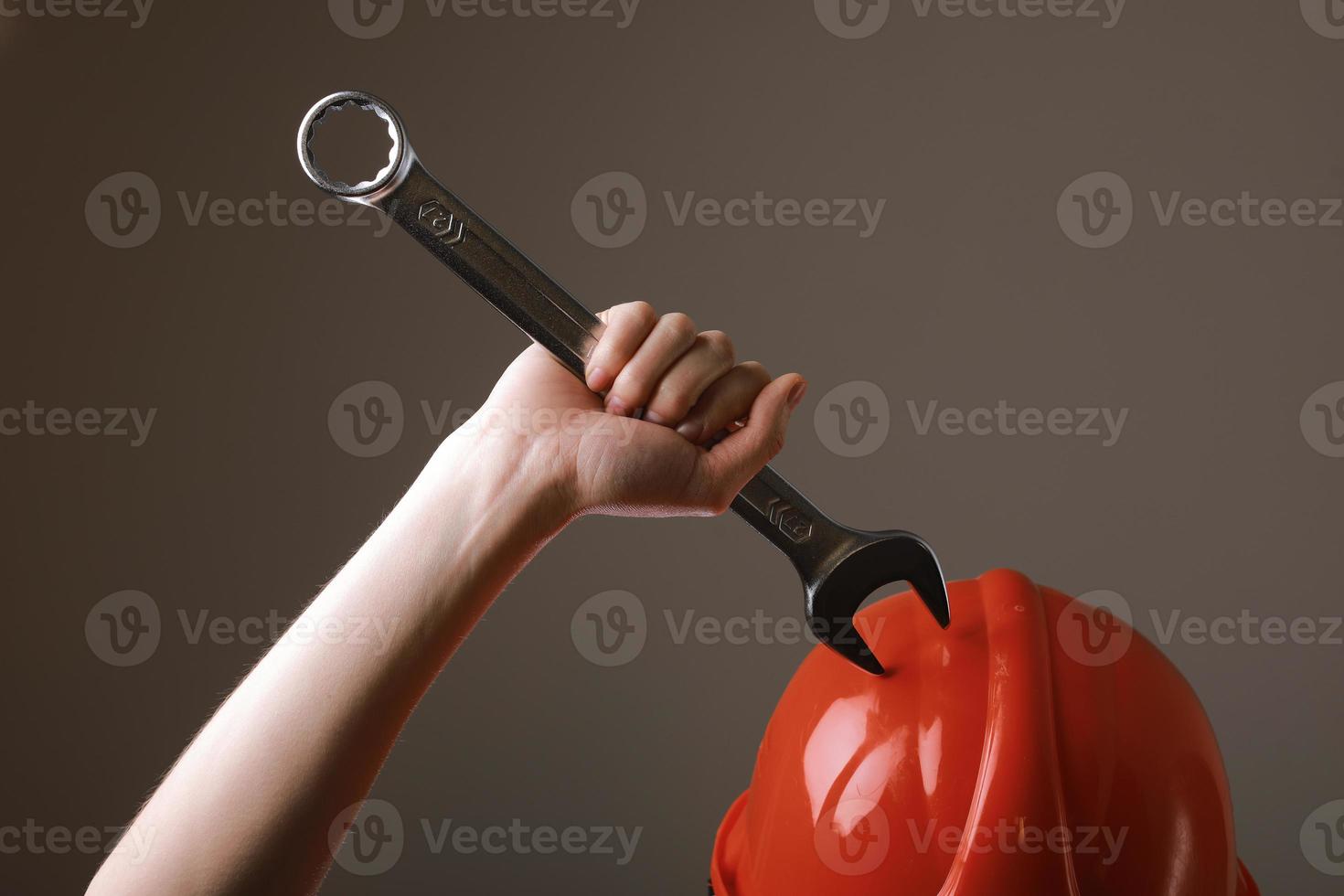 Big spanner in the woman's hand. Hand holds a wrench on a gray background. Combination wrench. Big chrome vanadium spanner in the hand. Women's work. photo