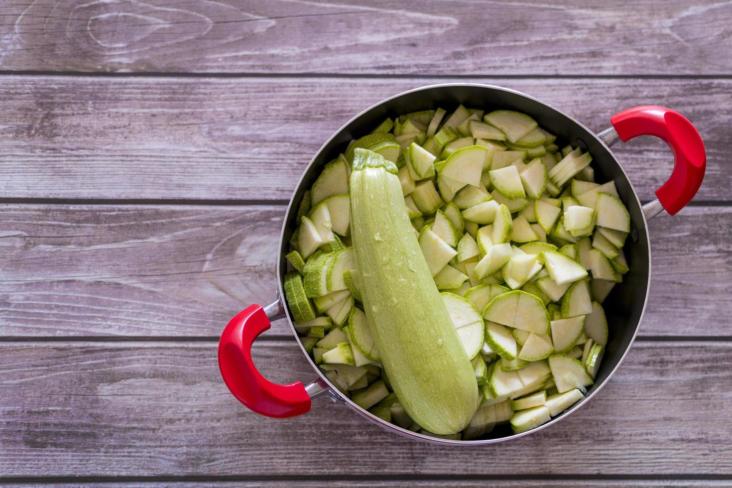 Fresh zucchini in cooking pot, on wooden background photo