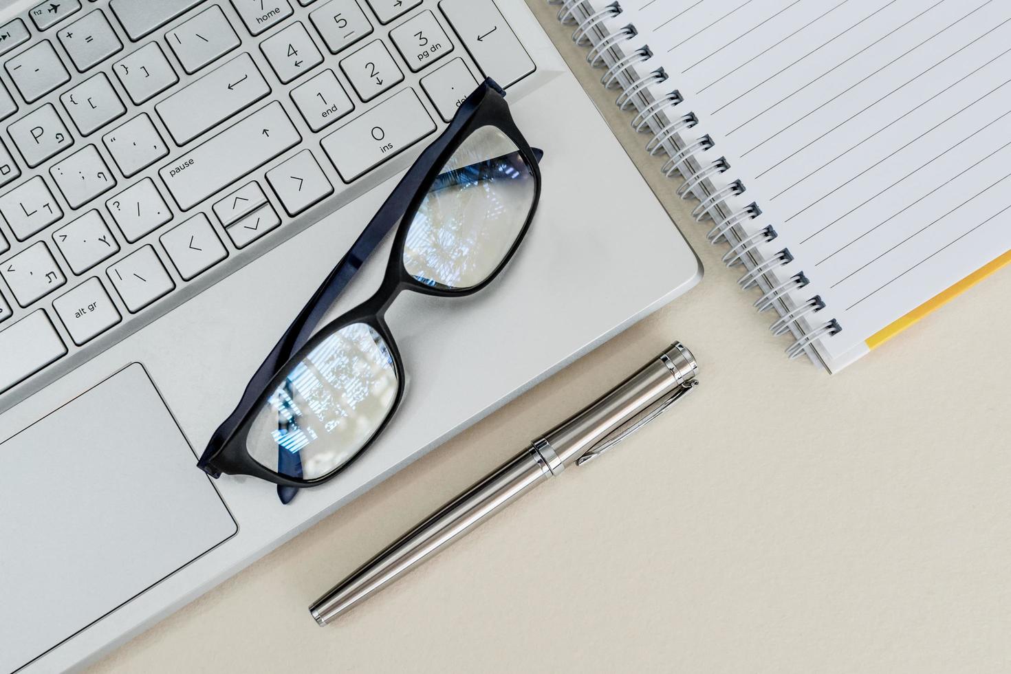 Top view of a desk with laptop, notebook, pen, and glasses photo