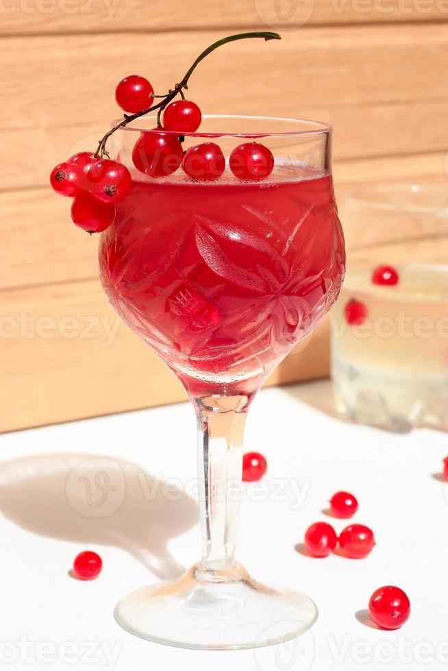 Jalea de vino champán rosado con grosella roja en un vaso, luz del día brillante, sobre fondo blanco y de madera foto