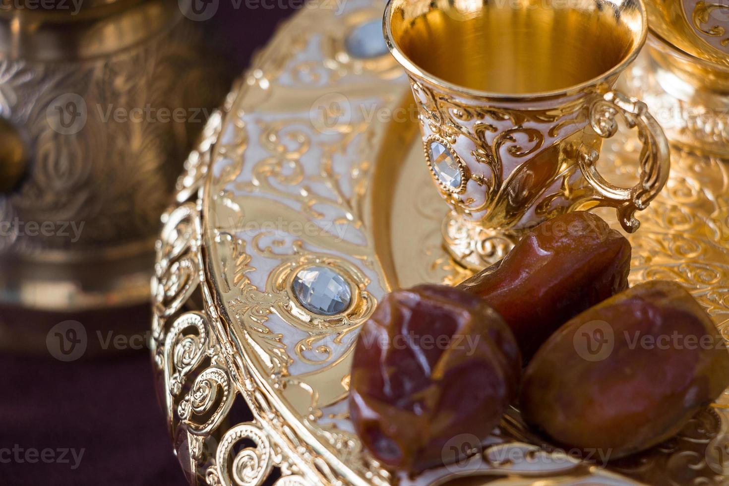 Still life with traditional golden Arabic coffee set with dallah, coffee pot, jezva, cup, and dates. Dark background. Horizontal photo