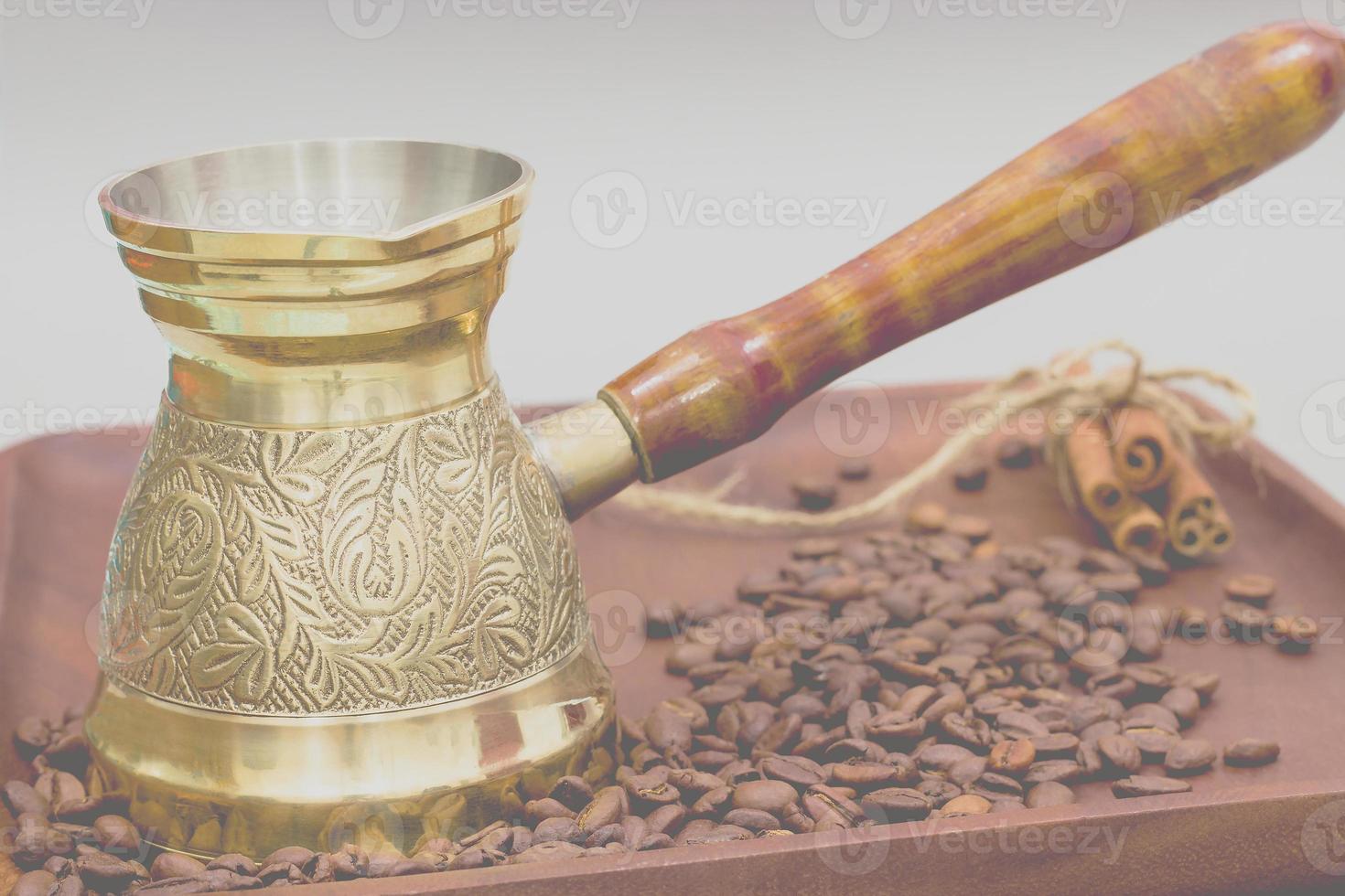 Copper coffee pot or ibrik with coffee beans and cinnamon sticks. On a wooden plate board. White background photo