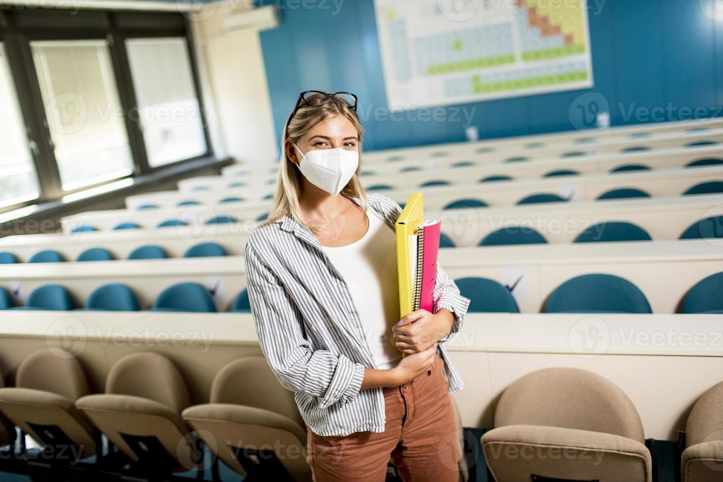 Female student wearing face protective medical mask for virus protection standing at lecture hall photo
