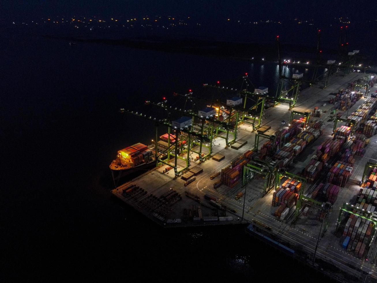 Jakarta, Indonesia 2021- Aerial view of Container ship loading and unloading in deep sea port, logistic import and export freight transportation by container ship in open sea at night photo