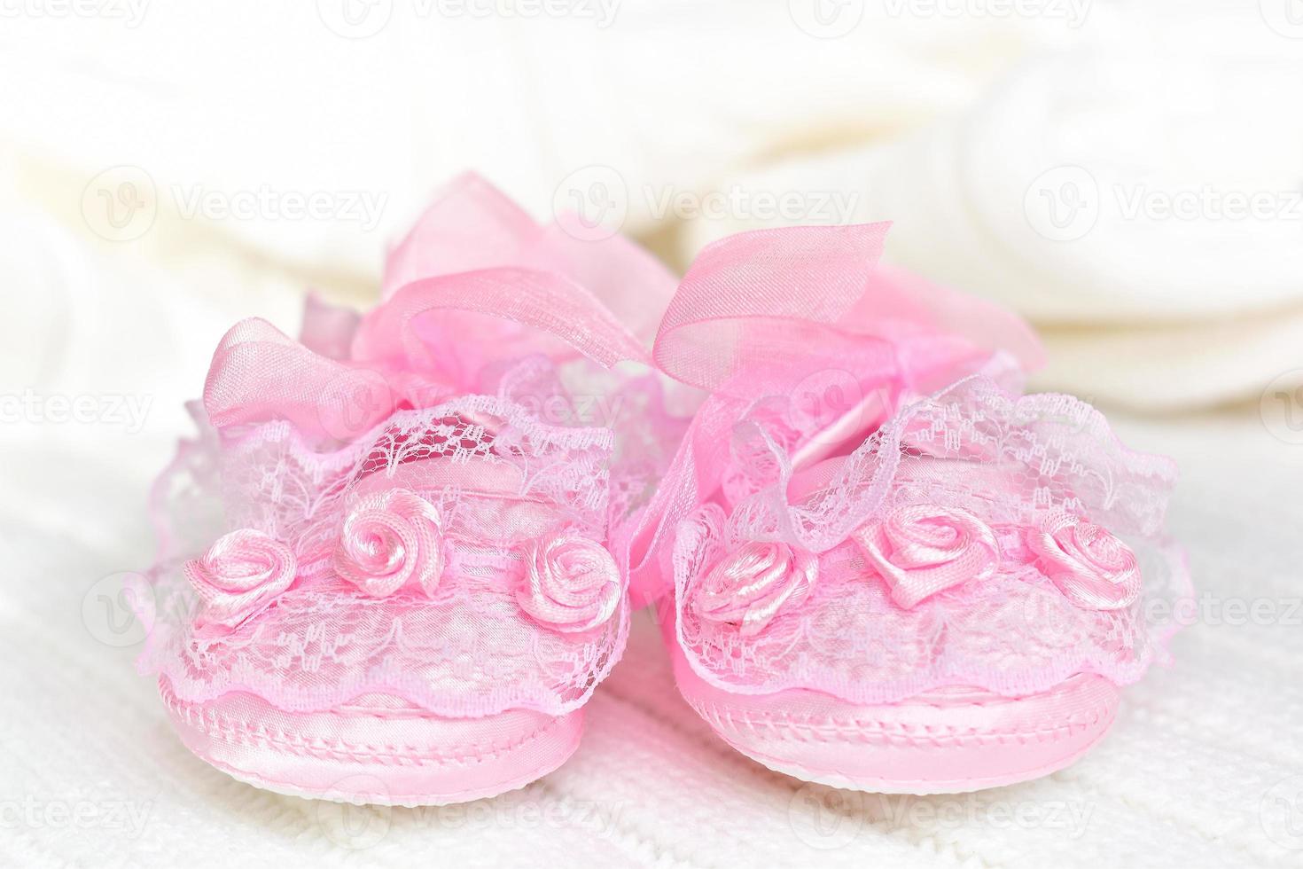 Pink baby booties on white crochet blanket. photo