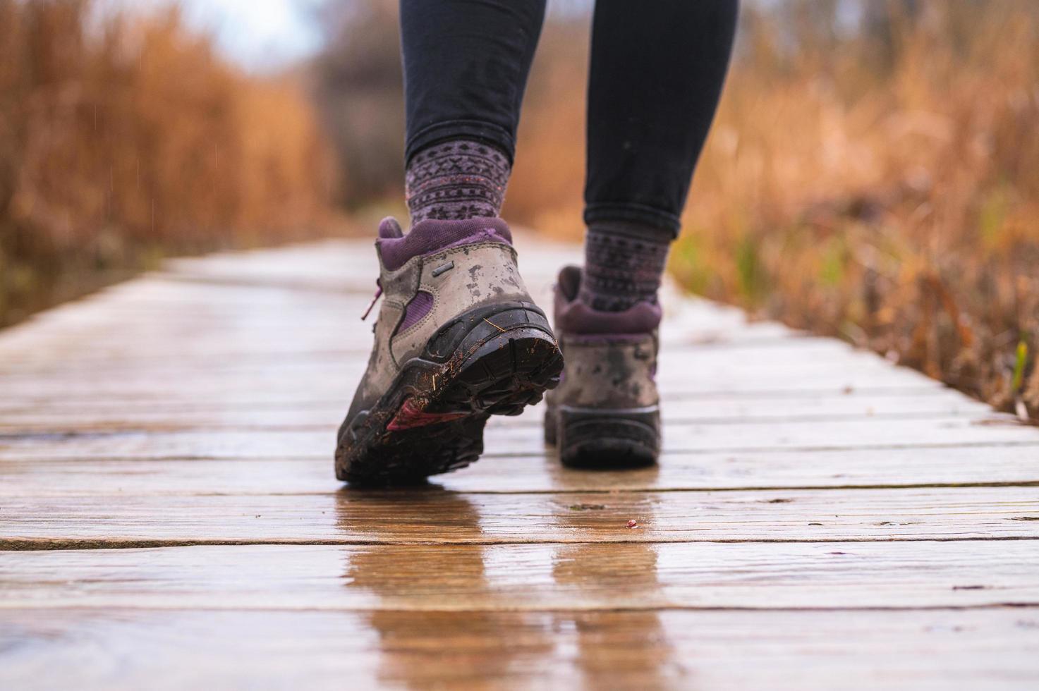 Los pies de la niña caminando sobre el malecón de madera con botas de montaña en un día lluvioso foto