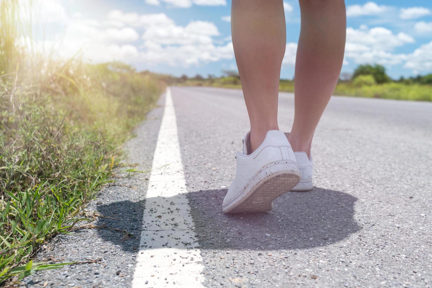 Mujer caminando por una pequeña carretera rural con fondo de cielo azul foto