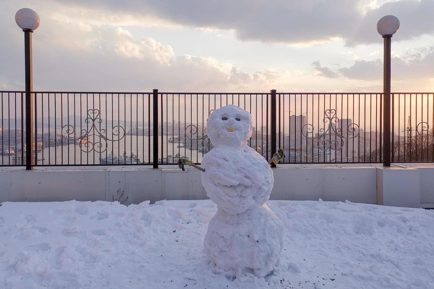 Snowman next to metal fence with cloudy orange sky photo