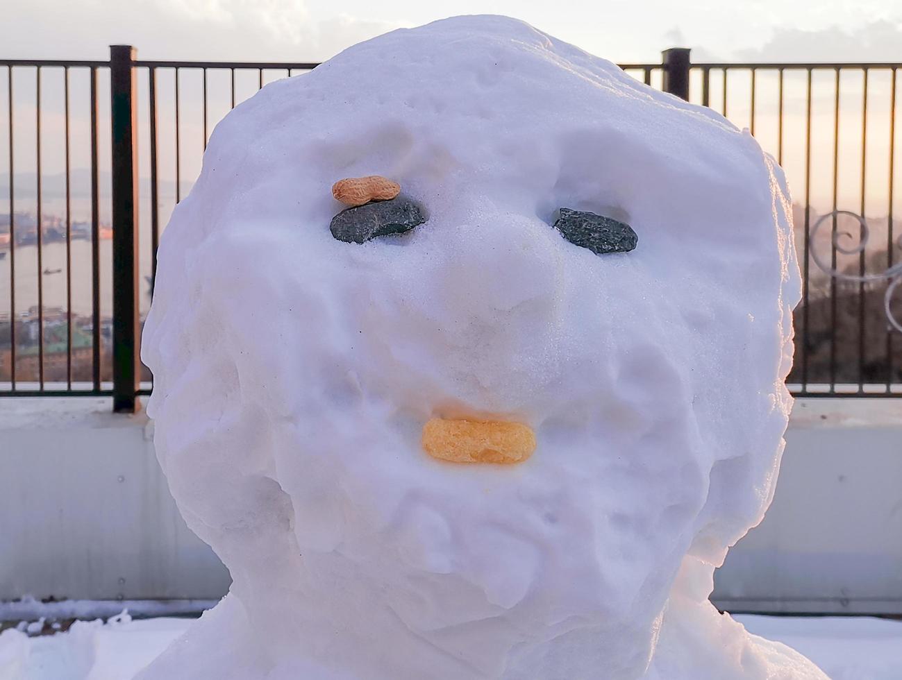 Close-up of the head of a snowman next to metal fence with cloudy orange sky photo