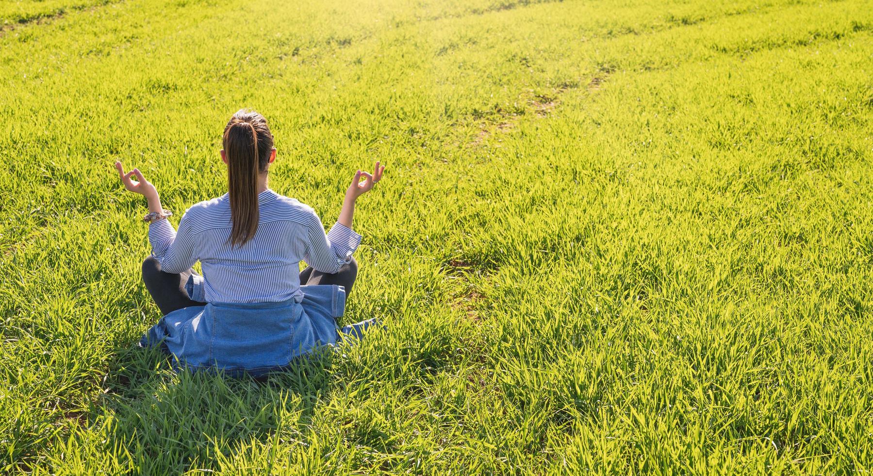 niña sentada en un prado verde en primavera con pose de meditación foto