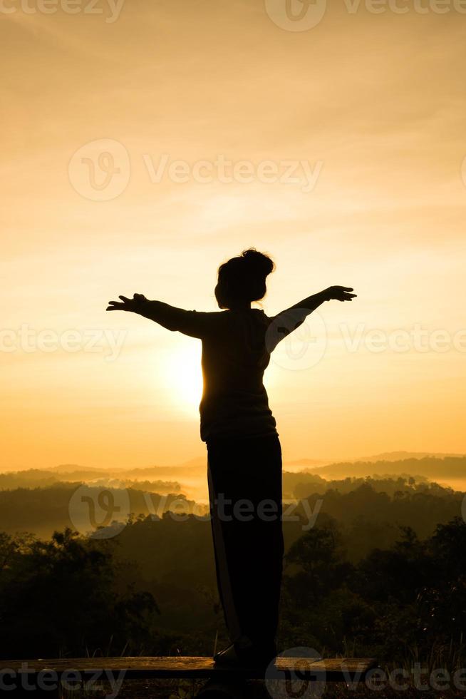 Silhouette of free cheering woman with open arms at mountain peak sunrise photo