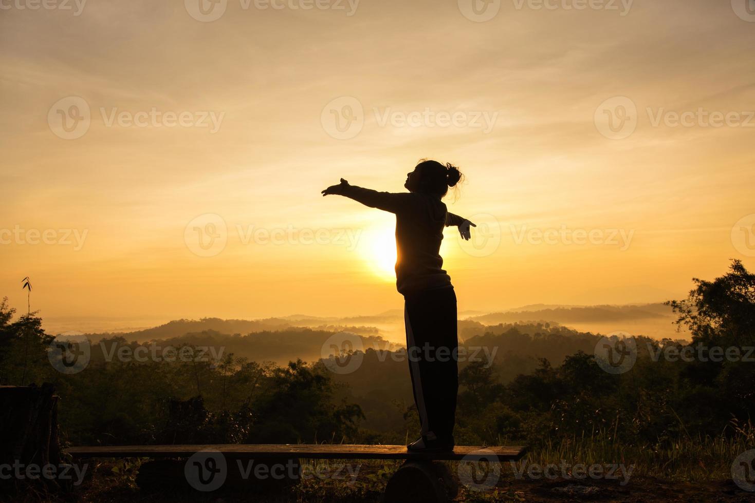 Silhouette of free cheering woman with open arms at mountain peak sunrise photo