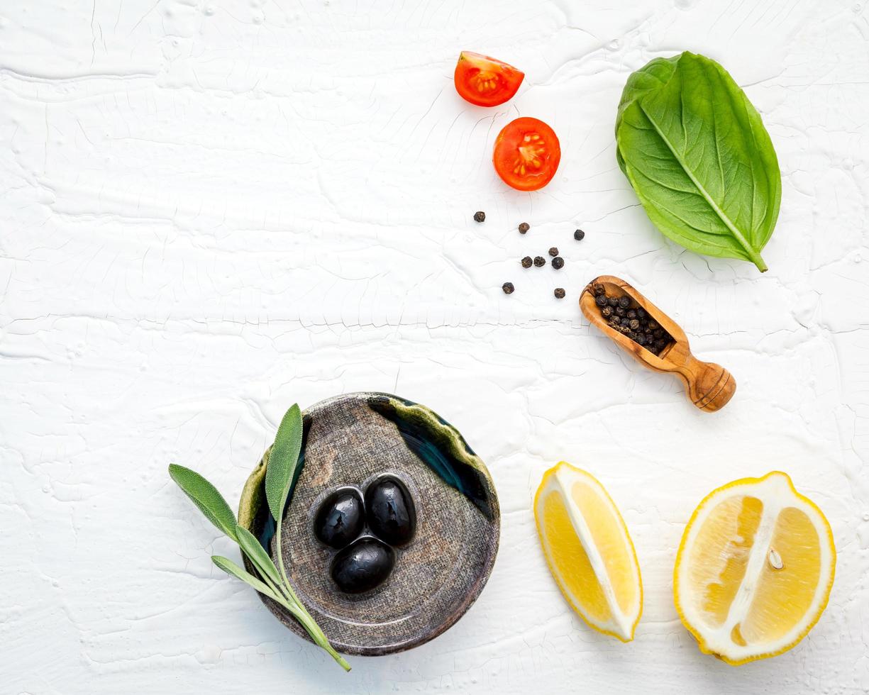 Fondo de alimentos con hierbas frescas, tomate, limón, pimienta negra, hojas de salvia, albahaca dulce y aceite de oliva sobre fondo de madera blanca foto