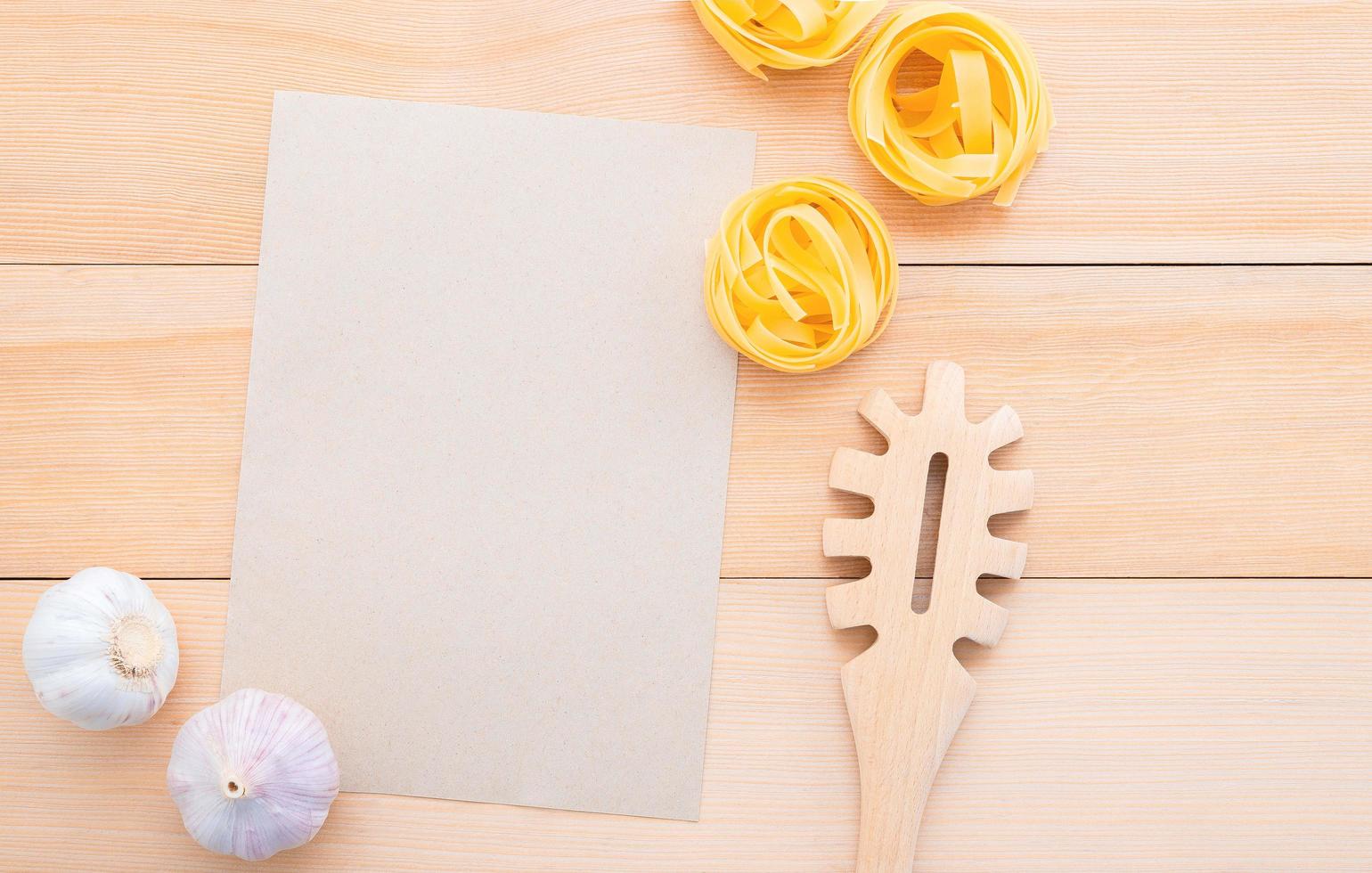 Cucharón de pasta y papel en blanco sobre fondo de madera foto