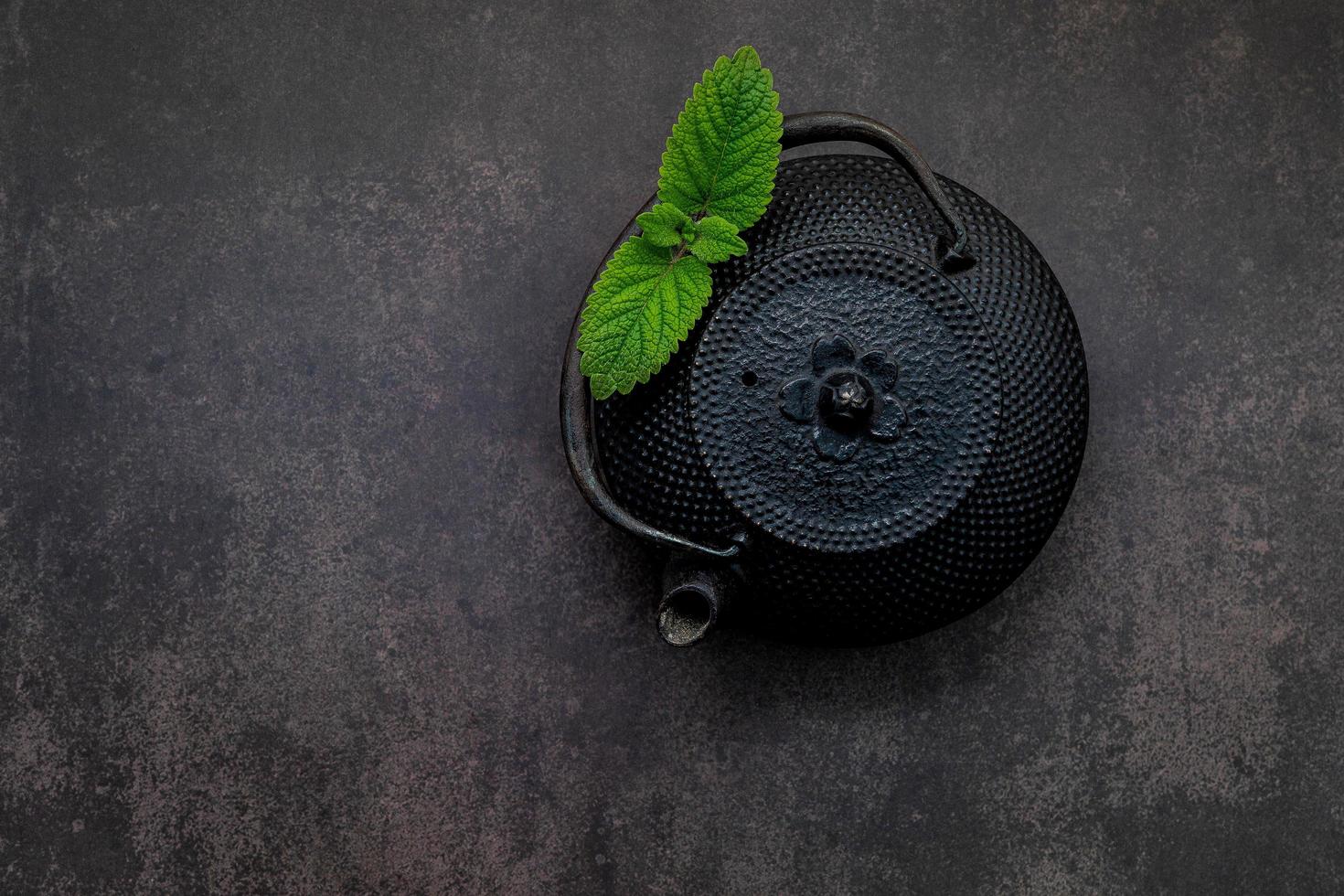 Black cast iron tea pot with herbal tea set up on dark stone background photo