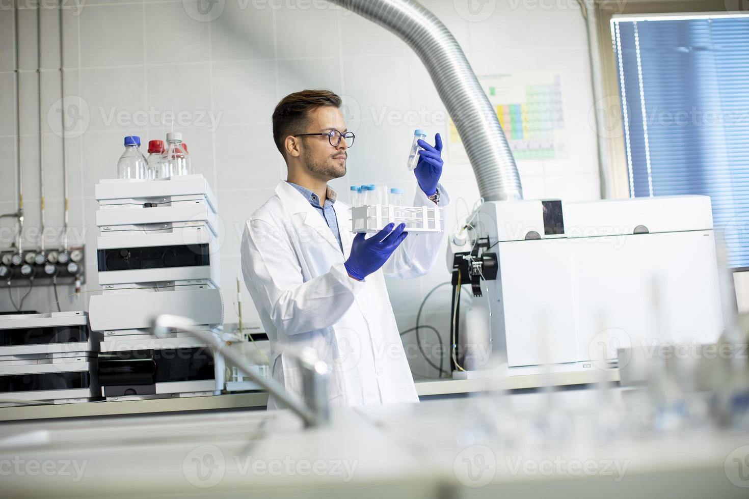 Joven investigador trabajando con muestras químicas en laboratorio con sistema HPLC y equipo de cromatografía foto