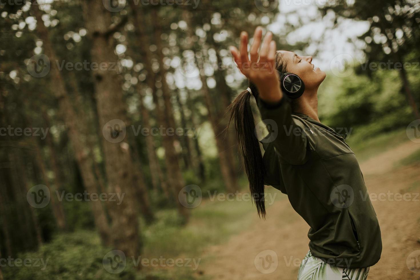 Mujer joven con auriculares predicando sus brazos en el bosque porque le gusta entrenar al aire libre foto