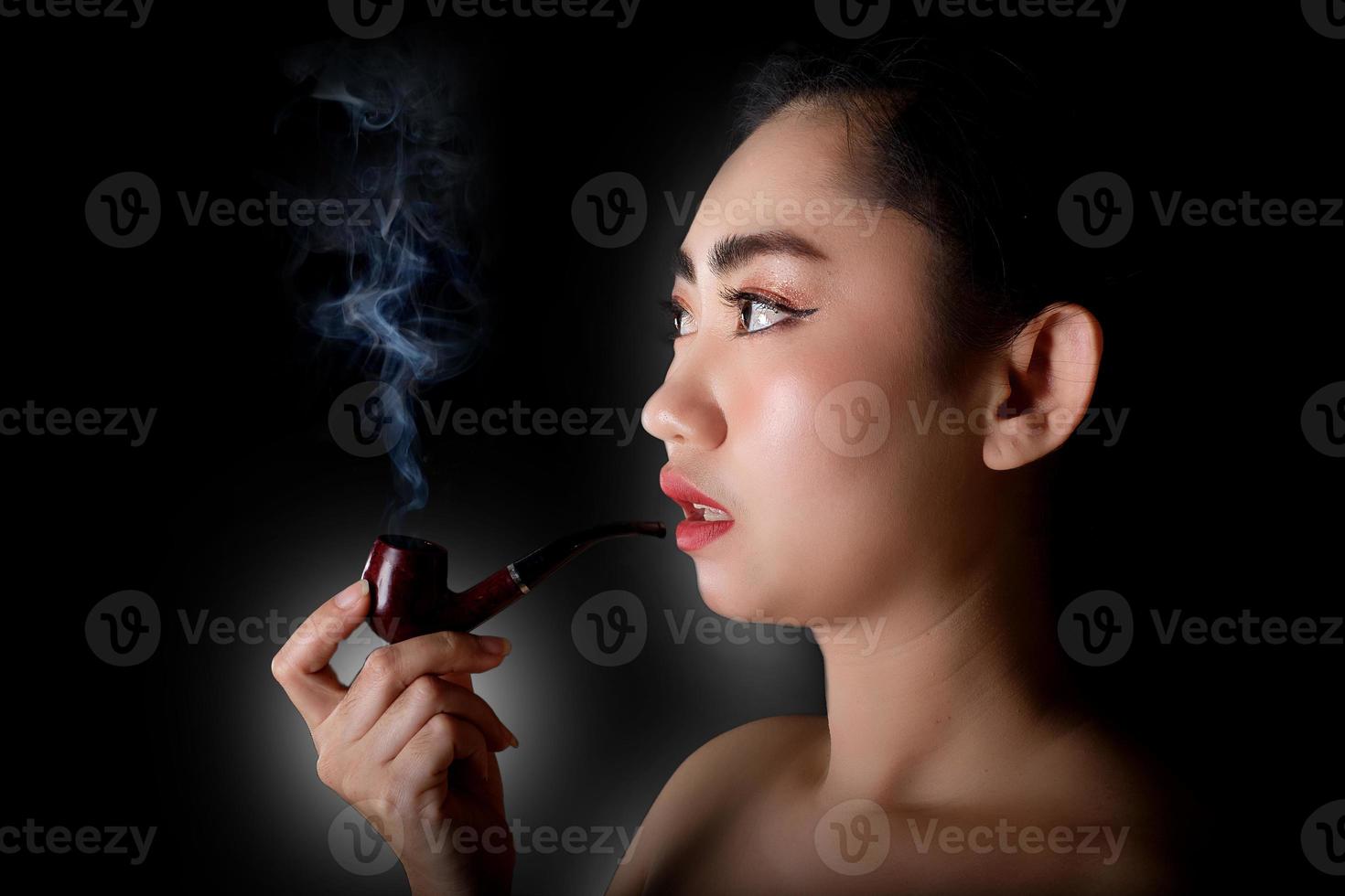 Woman smoking a pipe tobacco on black background photo