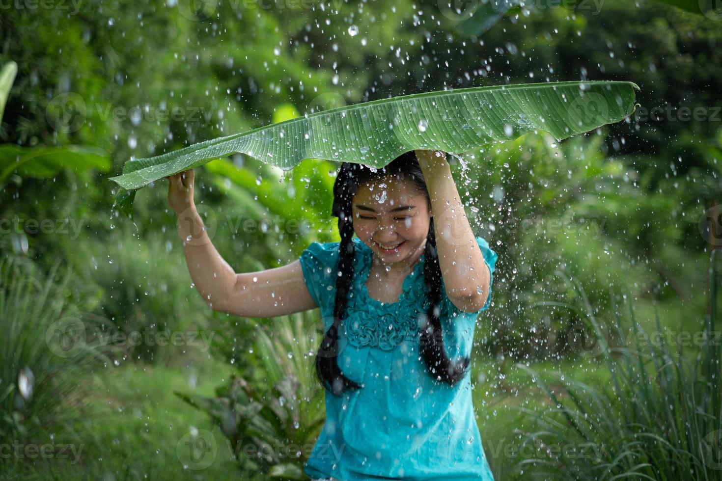 Mujer asiática con cabello negro sosteniendo una hoja de plátano bajo la lluvia foto