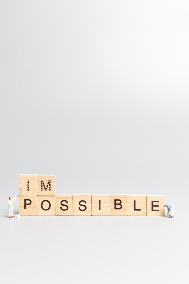 Miniature people, team of workers with the word Impossible in wooden letters with prefix un crossed-out, leaving the word possible photo