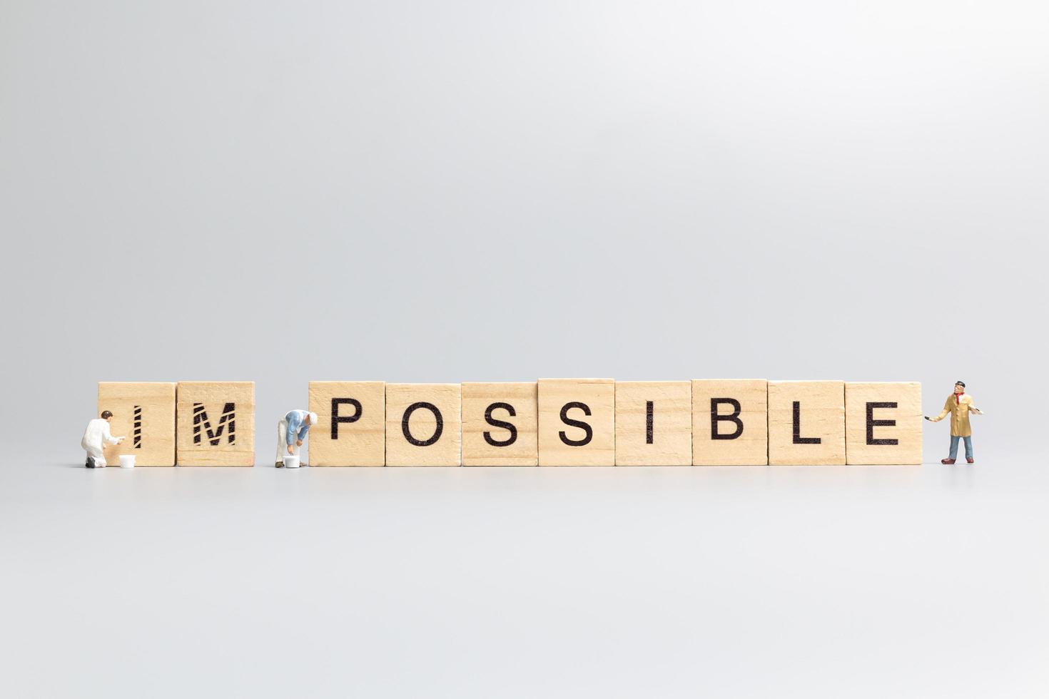 Miniature people, team of workers with the word Impossible in wooden letters with prefix un crossed-out, leaving the word possible photo
