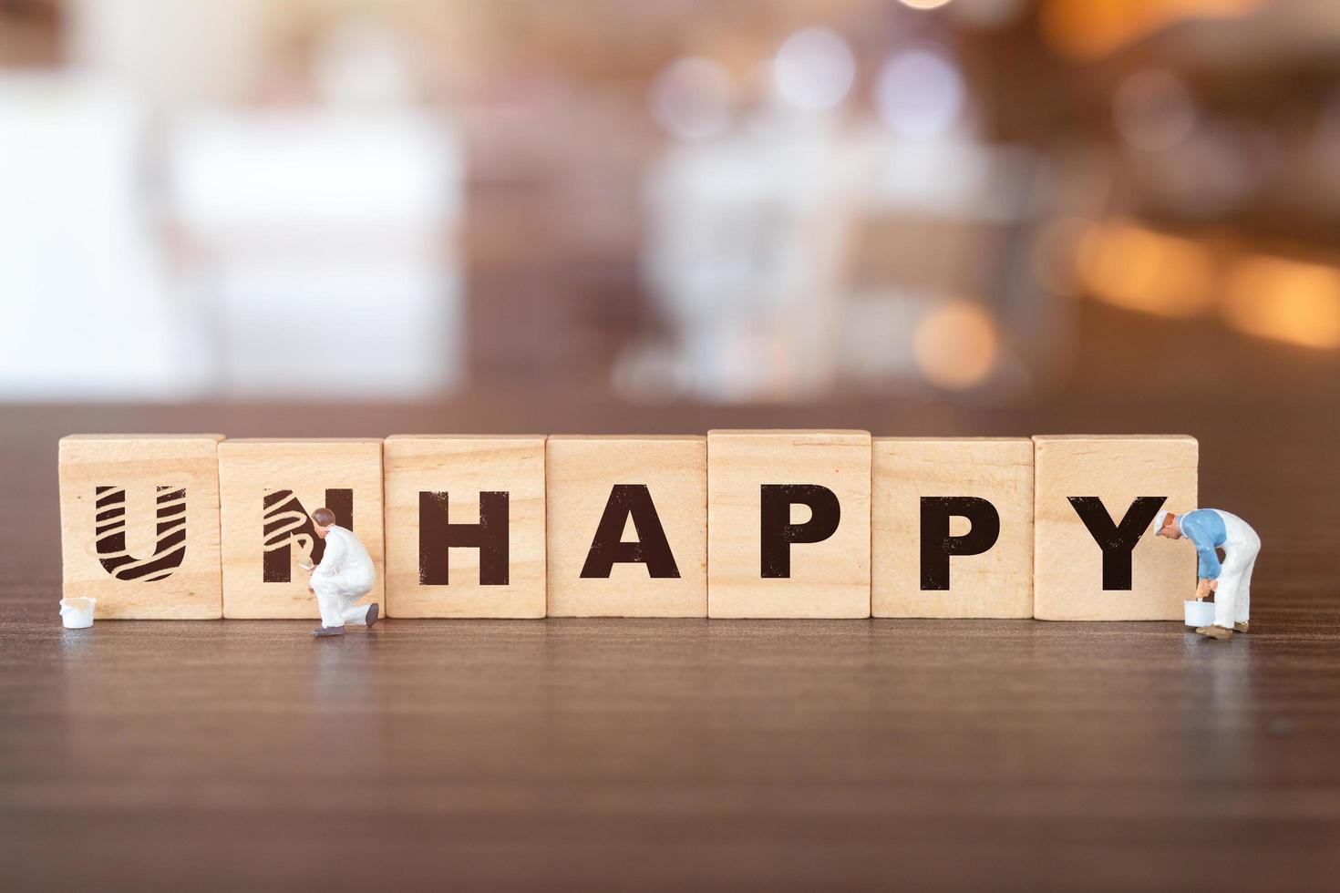 Miniature people, team of workers on wooden blocks with the word Unhappy with the prefix un- crossed-out, leaving the word happy photo