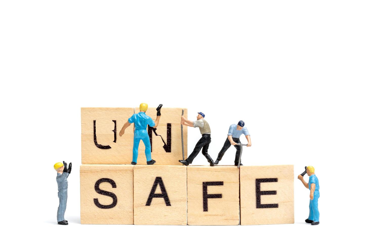 Miniature people, team of workers changing the word Unsafe turned into Safe on white background photo