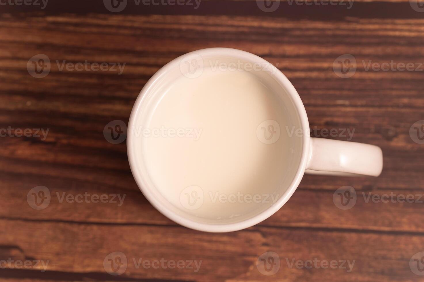 A white cup of milk sitting on a wooden table photo
