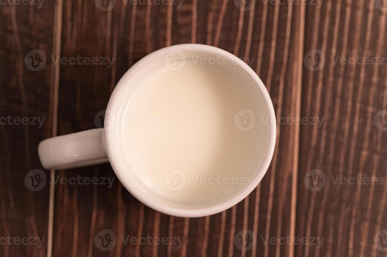 A white cup of milk sitting on a wooden table photo