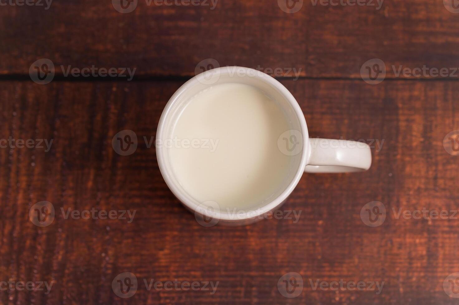 A white cup of milk sitting on a wooden table photo