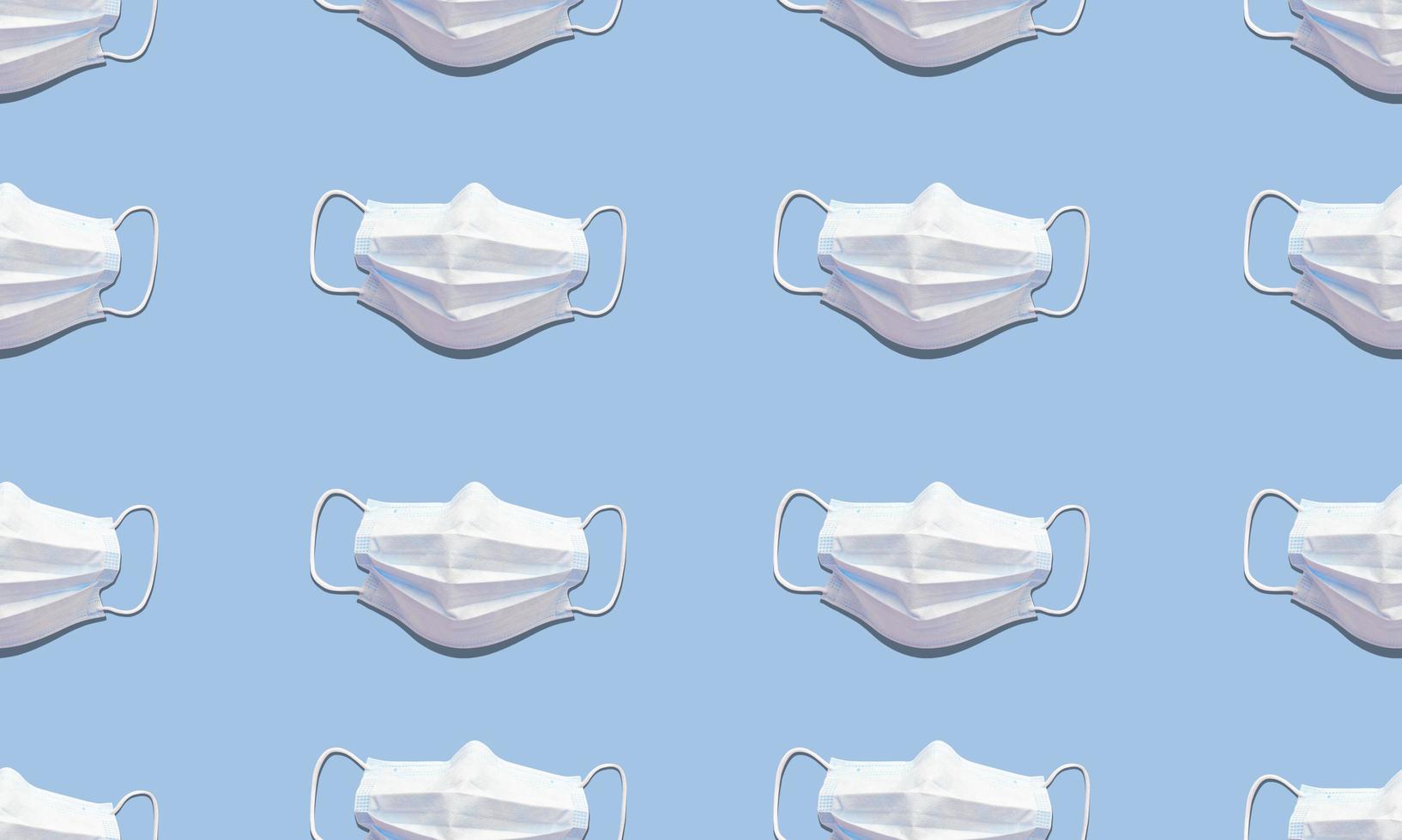 White medical masks on blue background. Trend seamless pattern with hard shadows. Flat lay stock photo. photo