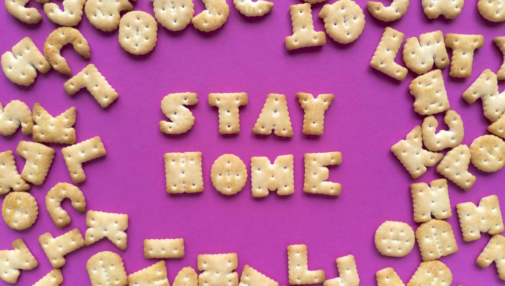 quedarse en casa. cita de cuarentena de galletas saladas sobre fondo rosa y letras dispersas. plano simple con textura pastel. Fotografía de archivo. foto